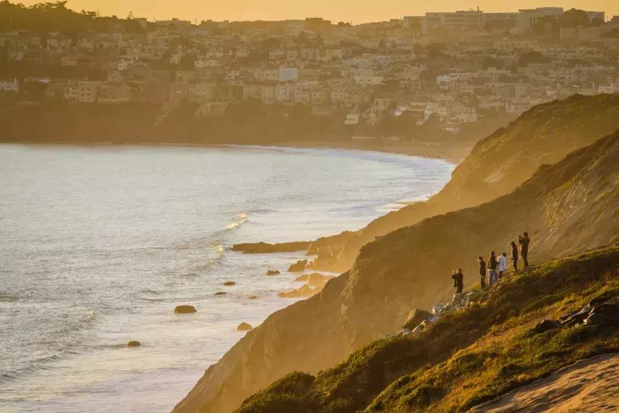 Un gruppo di persone sta su una scogliera di fronte all'oceano a guardare il tramonto nel Presidio di San Francisco.