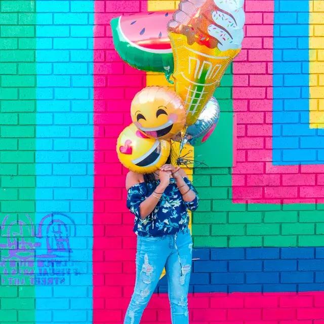 一位少女在多彩的壁画前拿着气球祝你生日快乐.