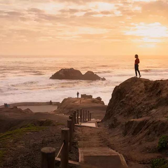 Due persone stanno sulle rocce che si affacciano sull'oceano ai Sutro Baths di San Francisco.